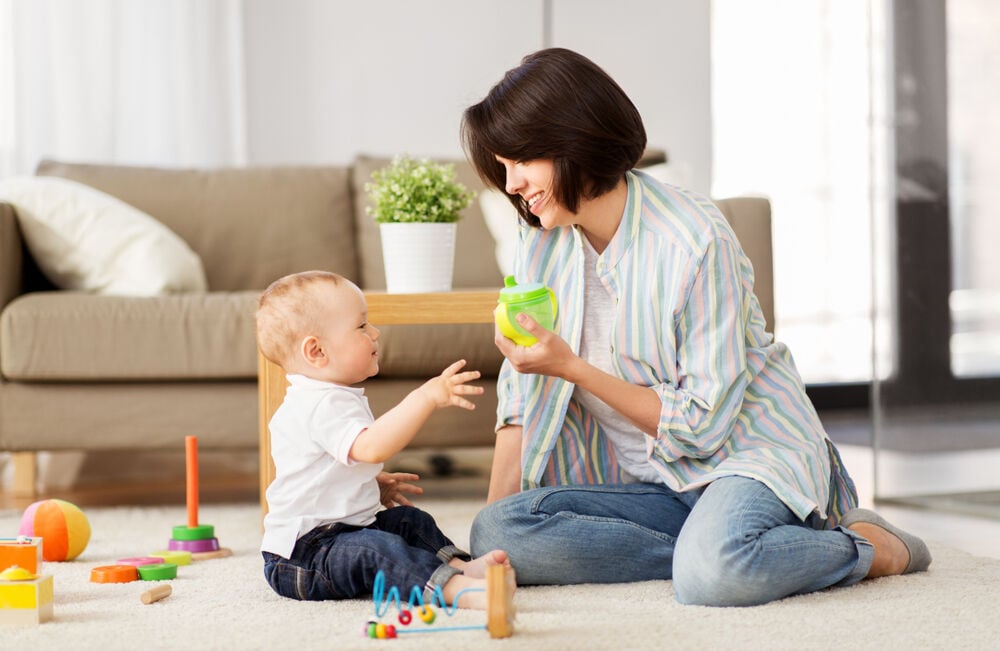 A woman gives her baby a sippy cup to wean the baby off the bottle A woman gives her baby a sippy cup to wean the baby off the bottle