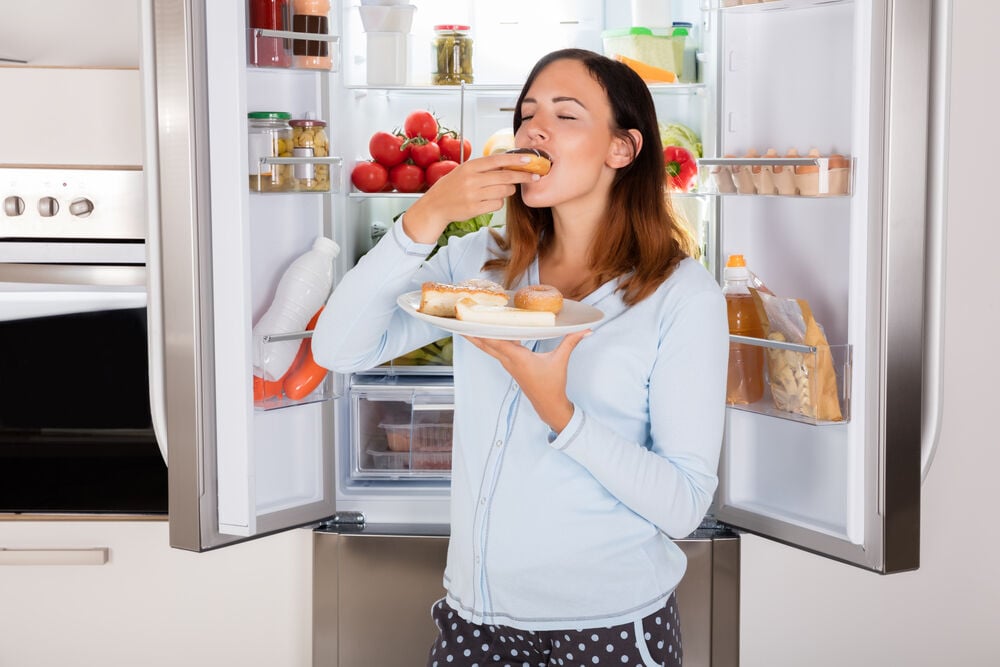 woman eating donut near refrigerator woman eating donut near refrigerator