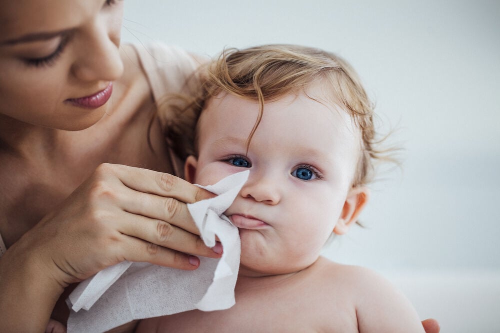 A woman wiping her baby's skin to prevent a rash from teething A woman wiping her baby's skin to prevent a rash from teething