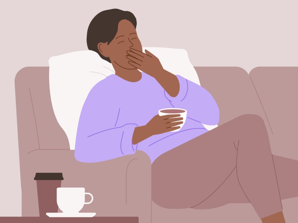 Sleepy woman with hot drink Tired woman sitting on the sofa
