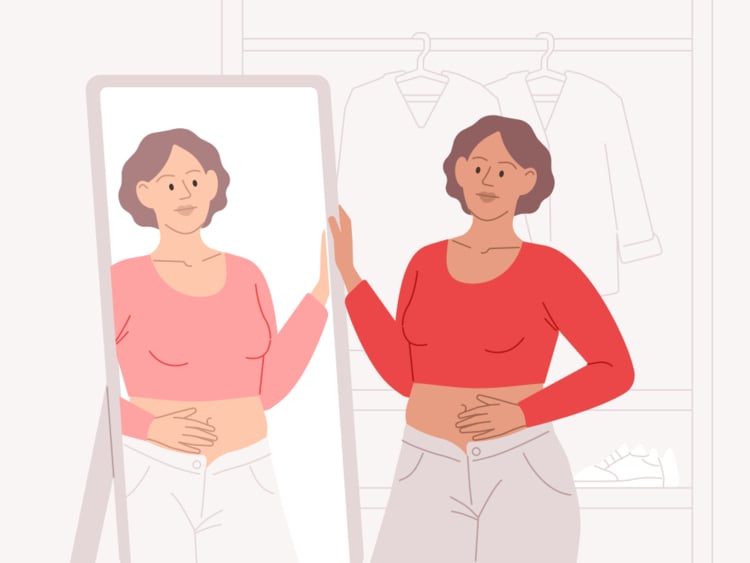 Woman looking in the mirror Woman with ovulation bloating looking in the mirror