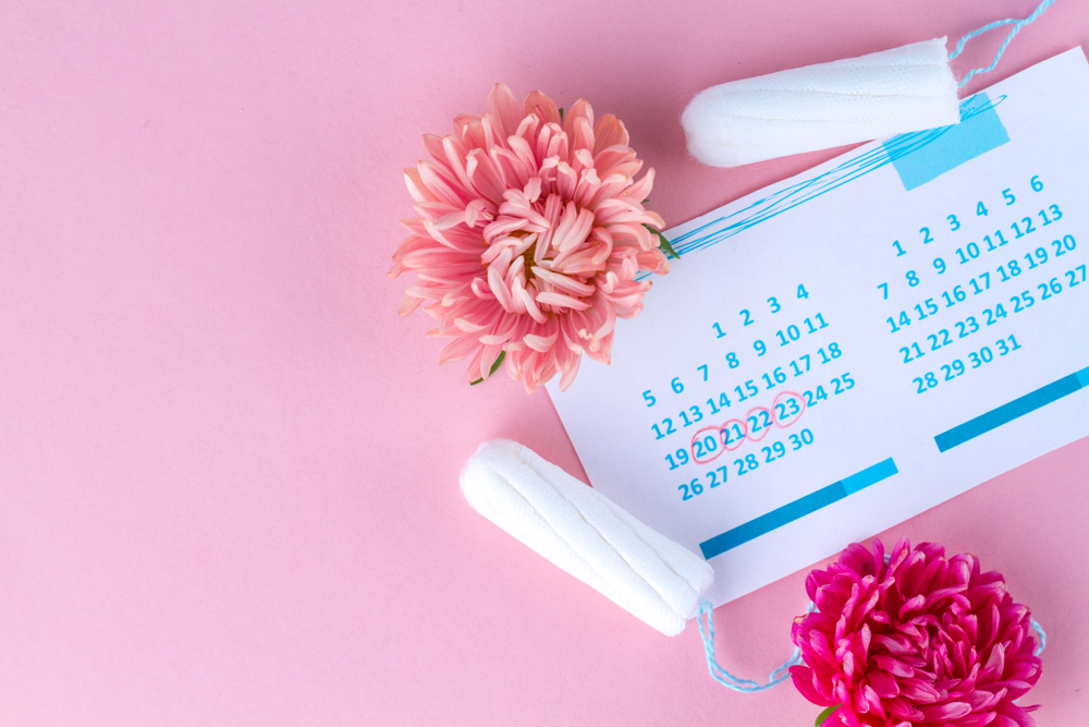 Tampons for menstruation, women's calendar and flowers on a pink background
