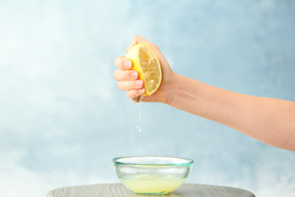 woman squeezing lemon juice into bowl on color background woman squeezing lemon juice into bowl on color background