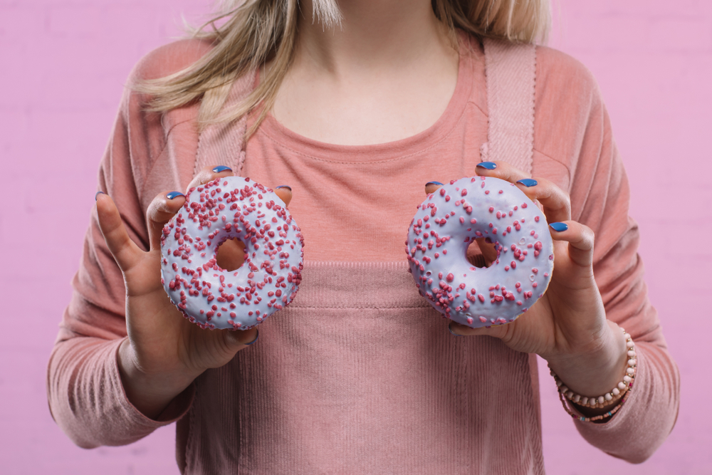 cropped shot of woman covering breast with glazed doughnuts cropped shot of woman covering breast with glazed doughnuts
