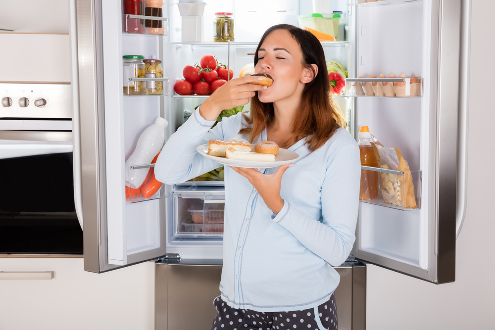 woman eating donut near refrigerator woman eating donut near refrigerator