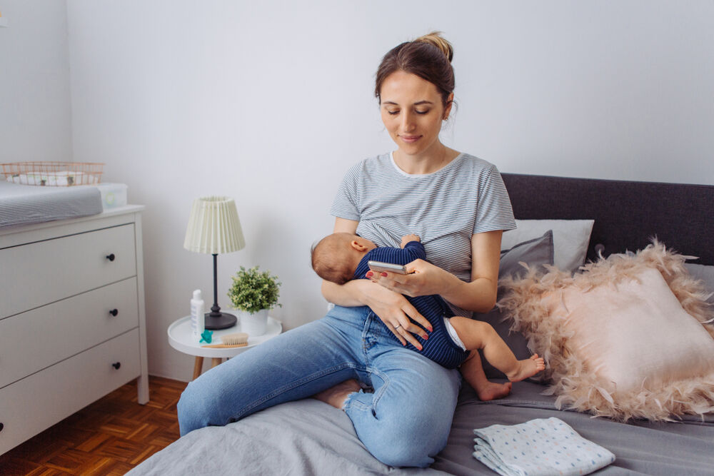 A woman uses a smartphone when her baby is going through a cluster-feeding episode