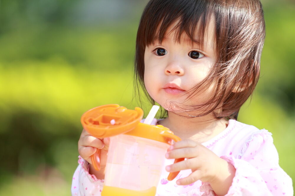 A baby drinking from a sippy cup with a straw
