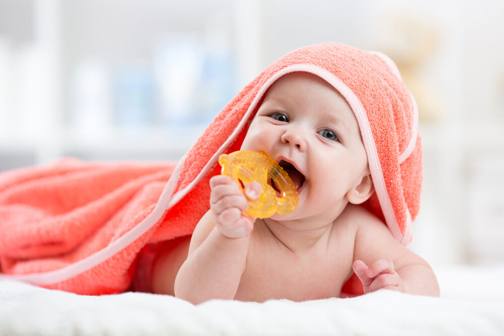 A baby teething at 3 months is holding a teething pacifier