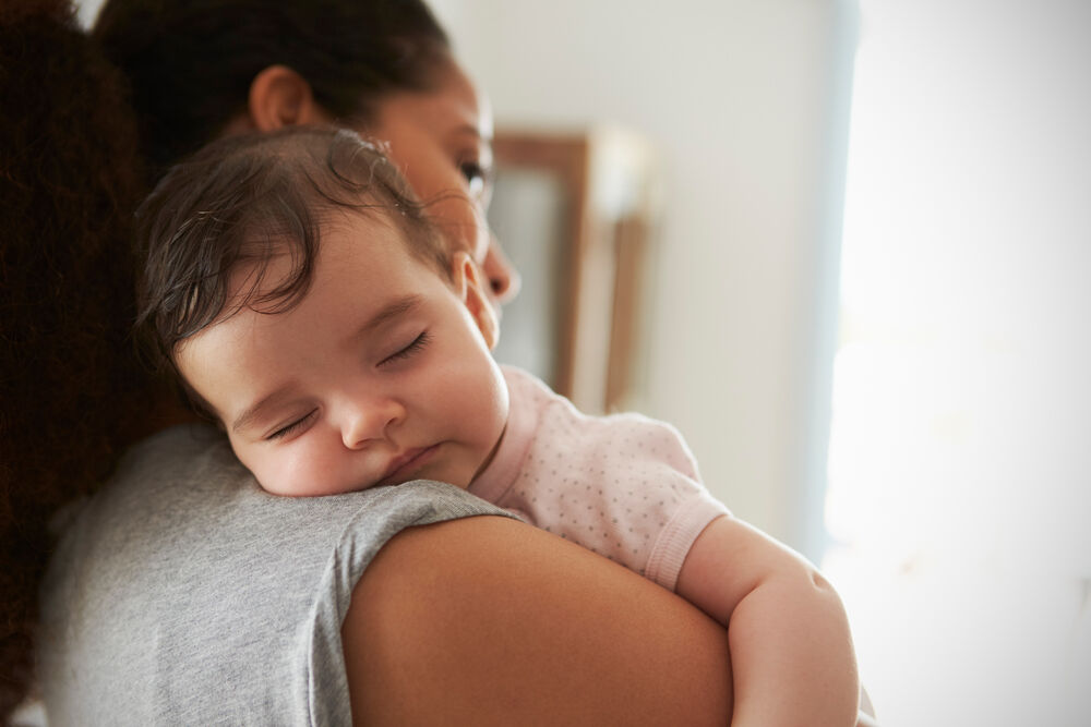 An 8-month-old baby sleeping on mother's shoulder