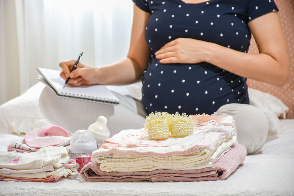 Pregnant woman is packing baby clothes for going to maternity hospital. 