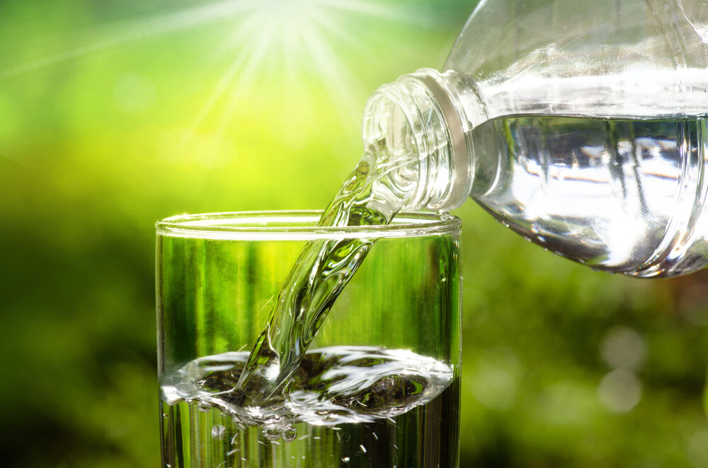 Drinking water pouring in to glass over sunlight and natural green background