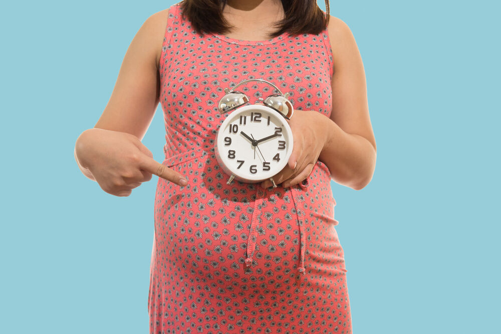 Pregnant woman holding clock. It's time. on blue background soft color