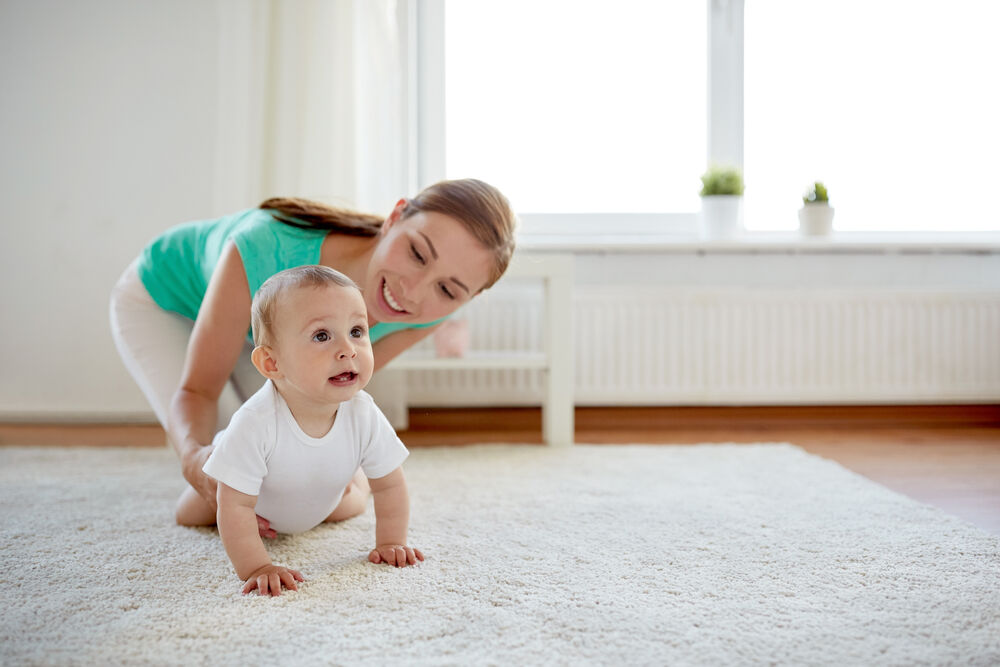 A woman is helping her baby to start crawling