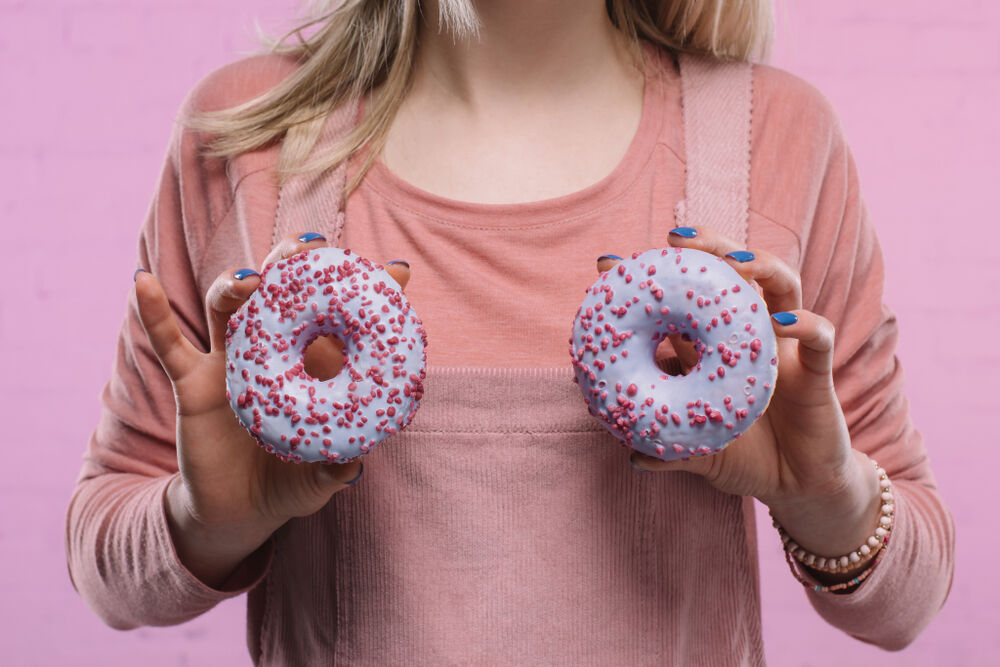 cropped shot of woman covering breast with glazed doughnuts