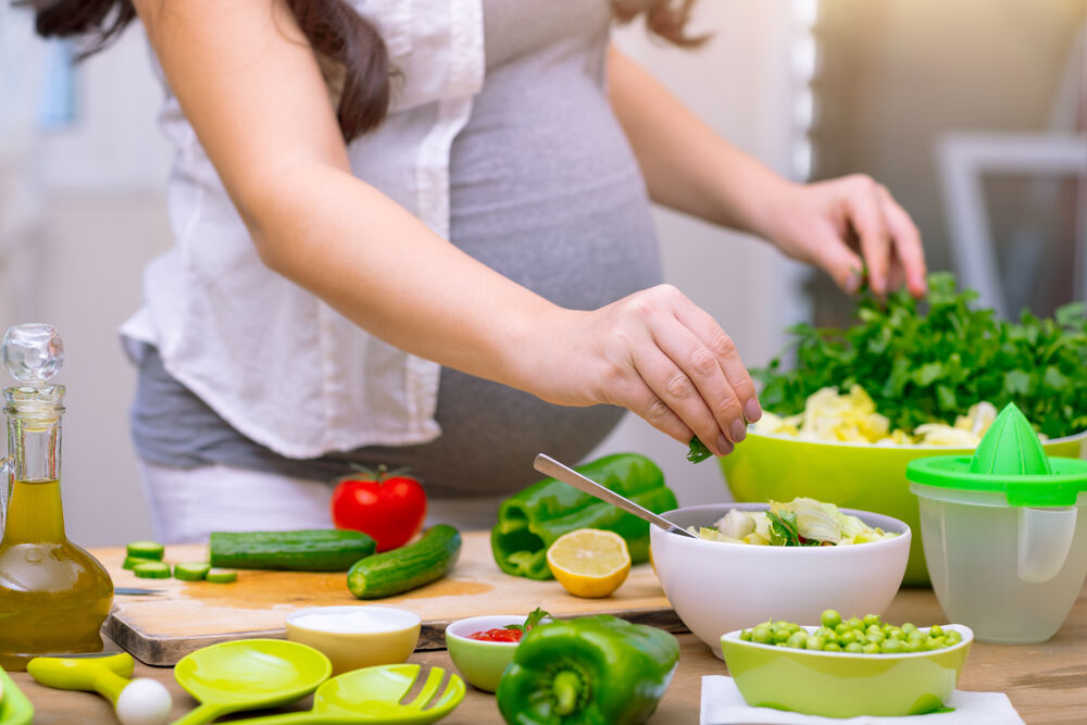 pregnant woman cooking at home, doing fresh green salad, eating many different vegetables