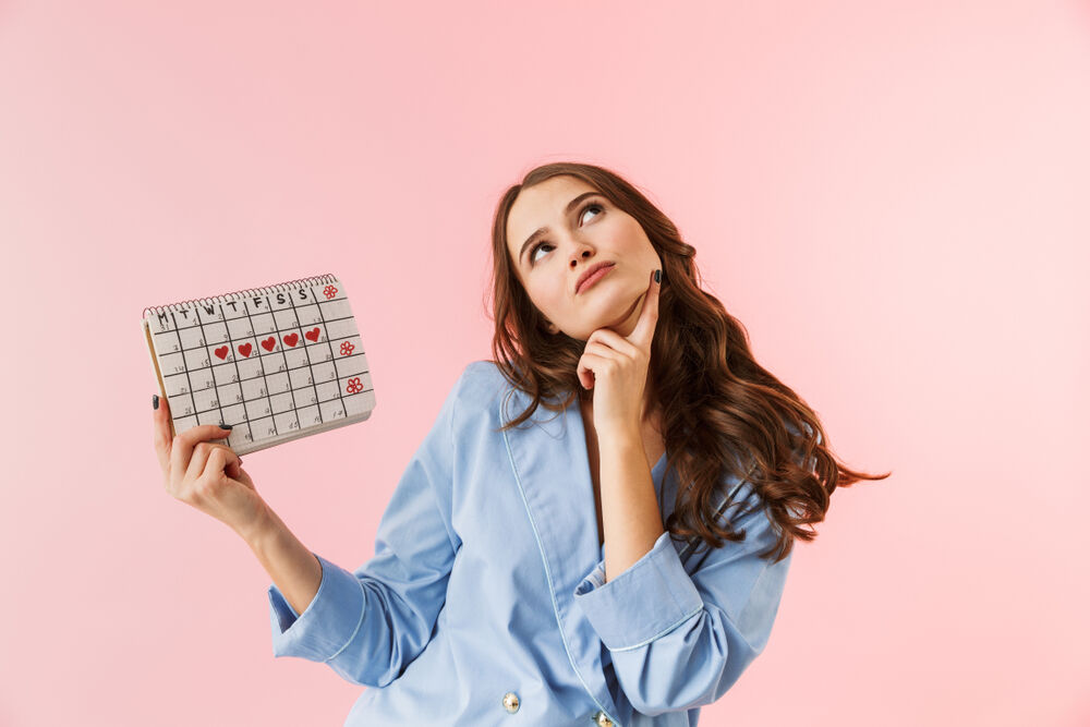 A confused woman holding a menstrual calendar wondering how late a period can be without being pregnant