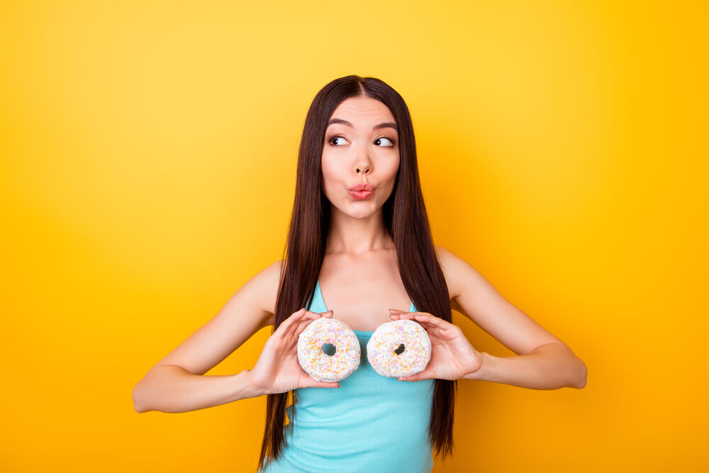 girl is holding donuts near her breasts