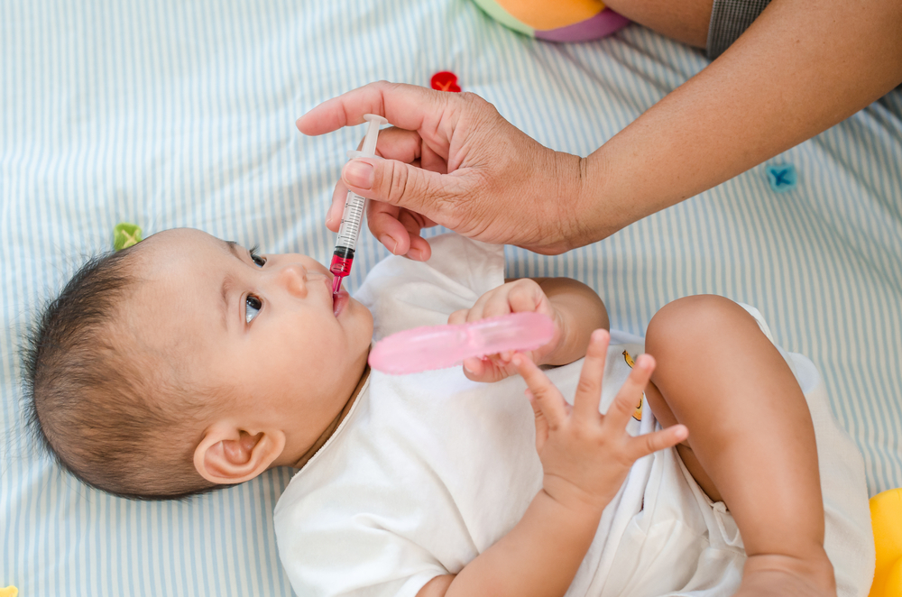 A mom giving liquid vitamins to her baby A mom giving liquid vitamins to her baby