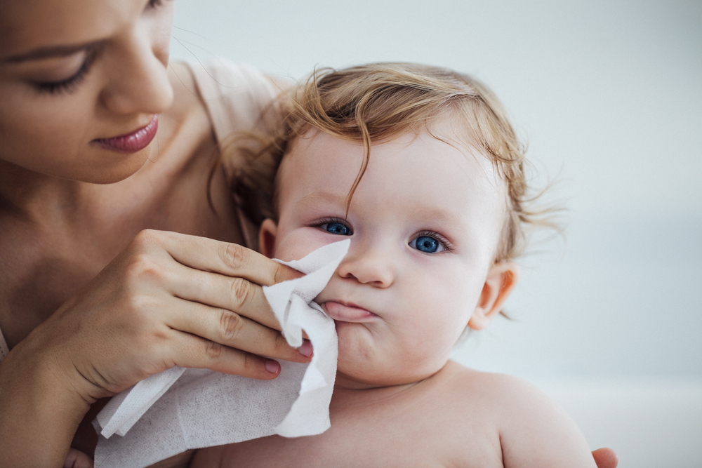 A woman wiping her baby's skin to prevent a rash from teething A woman wiping her baby's skin to prevent a rash from teething