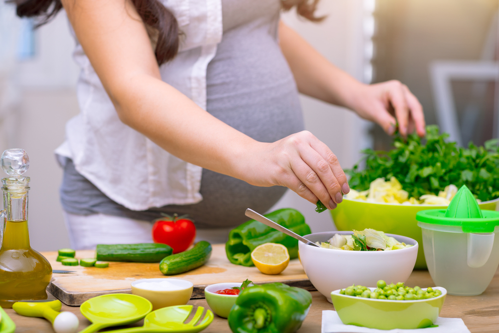 pregnant woman cooking at home, doing fresh green salad, eating many different vegetables pregnant woman cooking at home, doing fresh green salad, eating many different vegetables