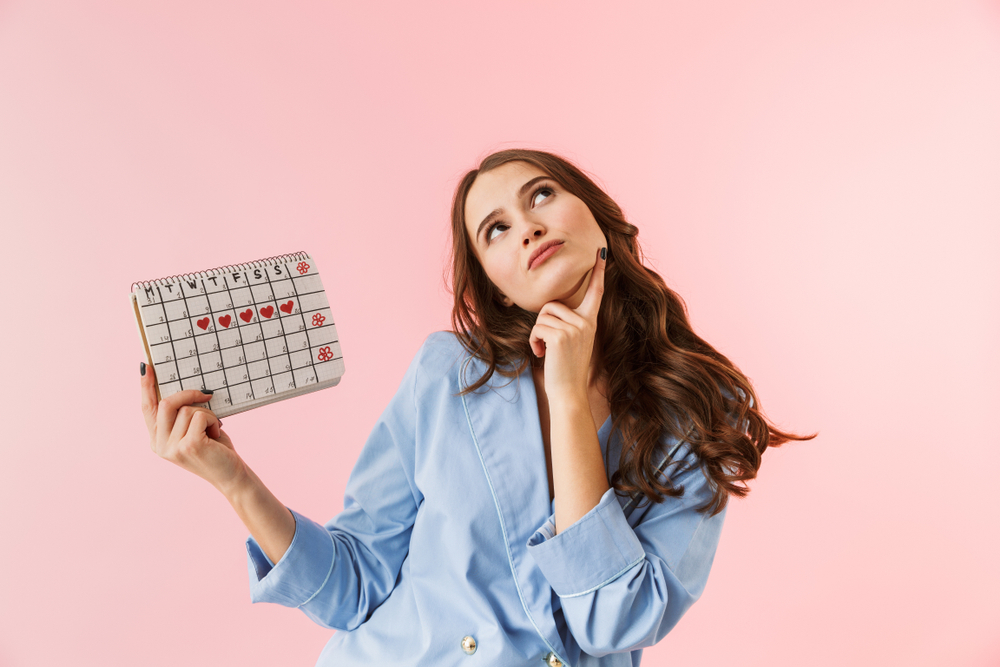 A confused woman holding a menstrual calendar wondering how late a period can be without being pregnant A confused woman holding a menstrual calendar wondering how late a period can be without being pregnant