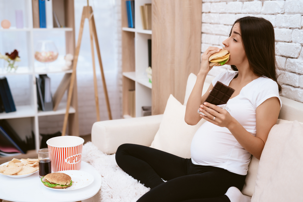 girl eating a hamburger and chocolate sitting on the couch. girl eating a hamburger and chocolate sitting on the couch.