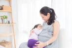 A woman breastfeeding her baby while being preganant