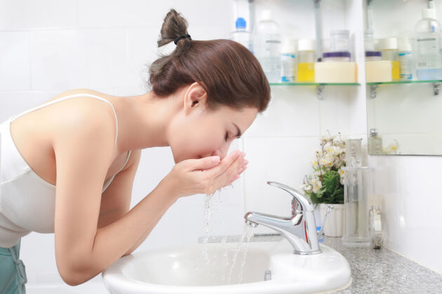 Woman washing her face with water above bathroom sink to avoid acne before period